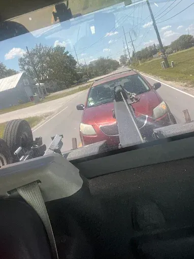 A red car being towed by a tow truck on a road.