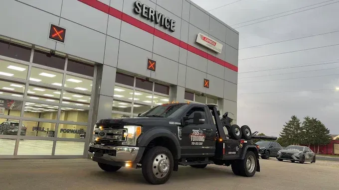 Tow truck in front of a service center; gray vehicle, red and white building facade, overcast sky.