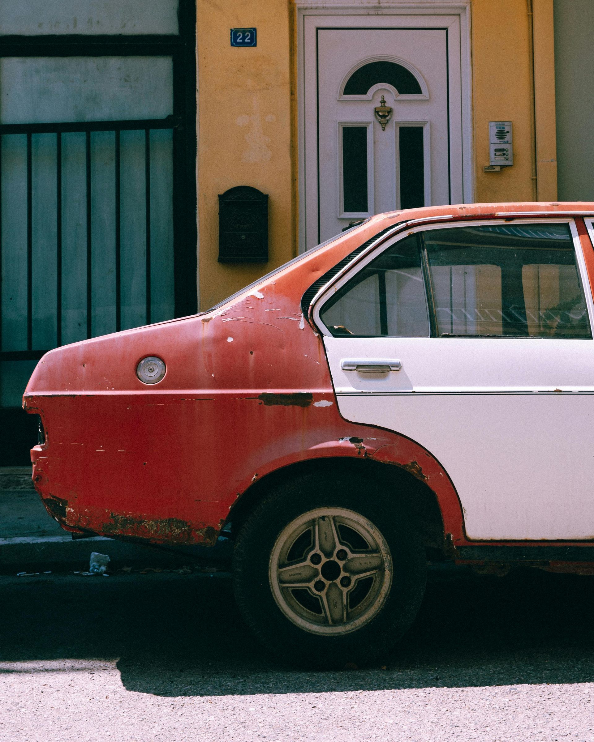 Red and white car parked on a street in front of a yellow building with a white door.