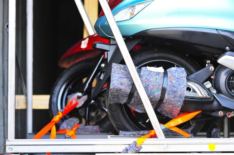 A blue and black scooter secured in a shipping crate with straps and padding.