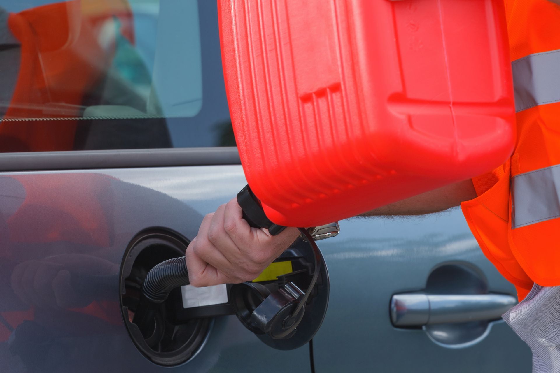 Person in orange vest pouring fuel from a red container into a car's gas tank.