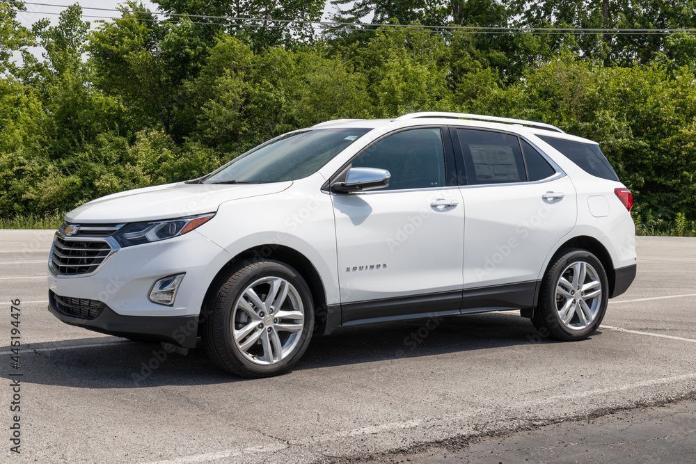A white Chevrolet Equinox SUV parked on a paved lot with green trees in the background.