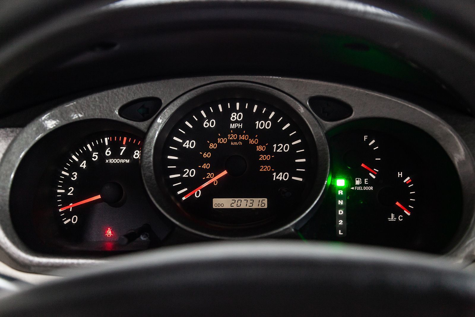 A vehicle instrument cluster at night, showing a speedometer, tachometer, fuel gauge, and gear indicator set to Park.
