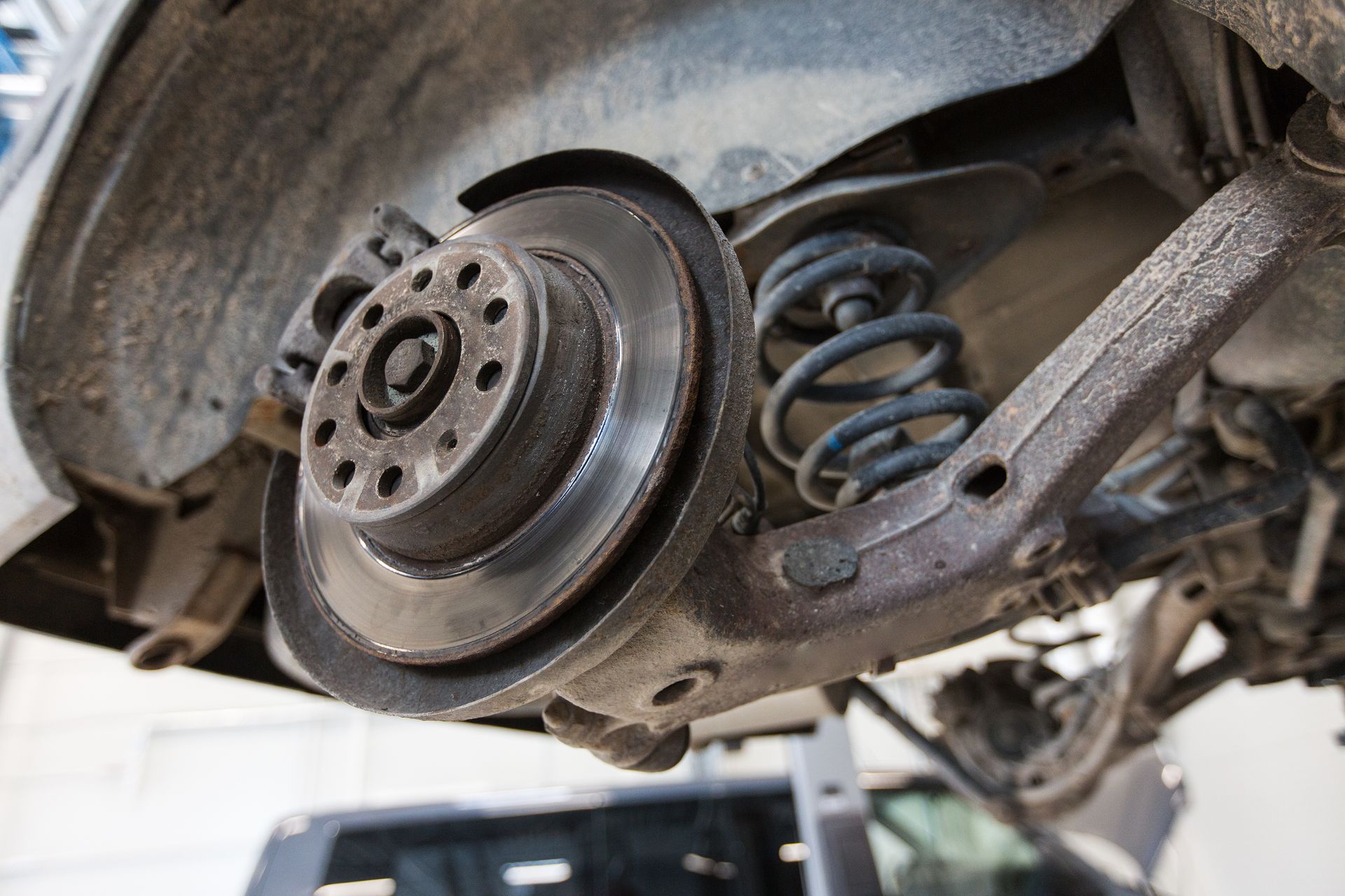 Car wheel hub and brake rotor exposed under a vehicle on a lift in a repair shop