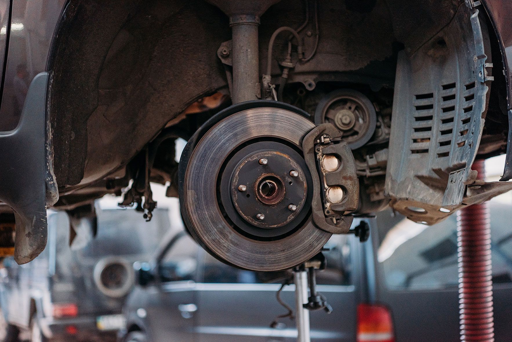 Close-up of a car's wheel hub and brake disc assembly with a brake caliper attached, viewed in an auto repair shop.