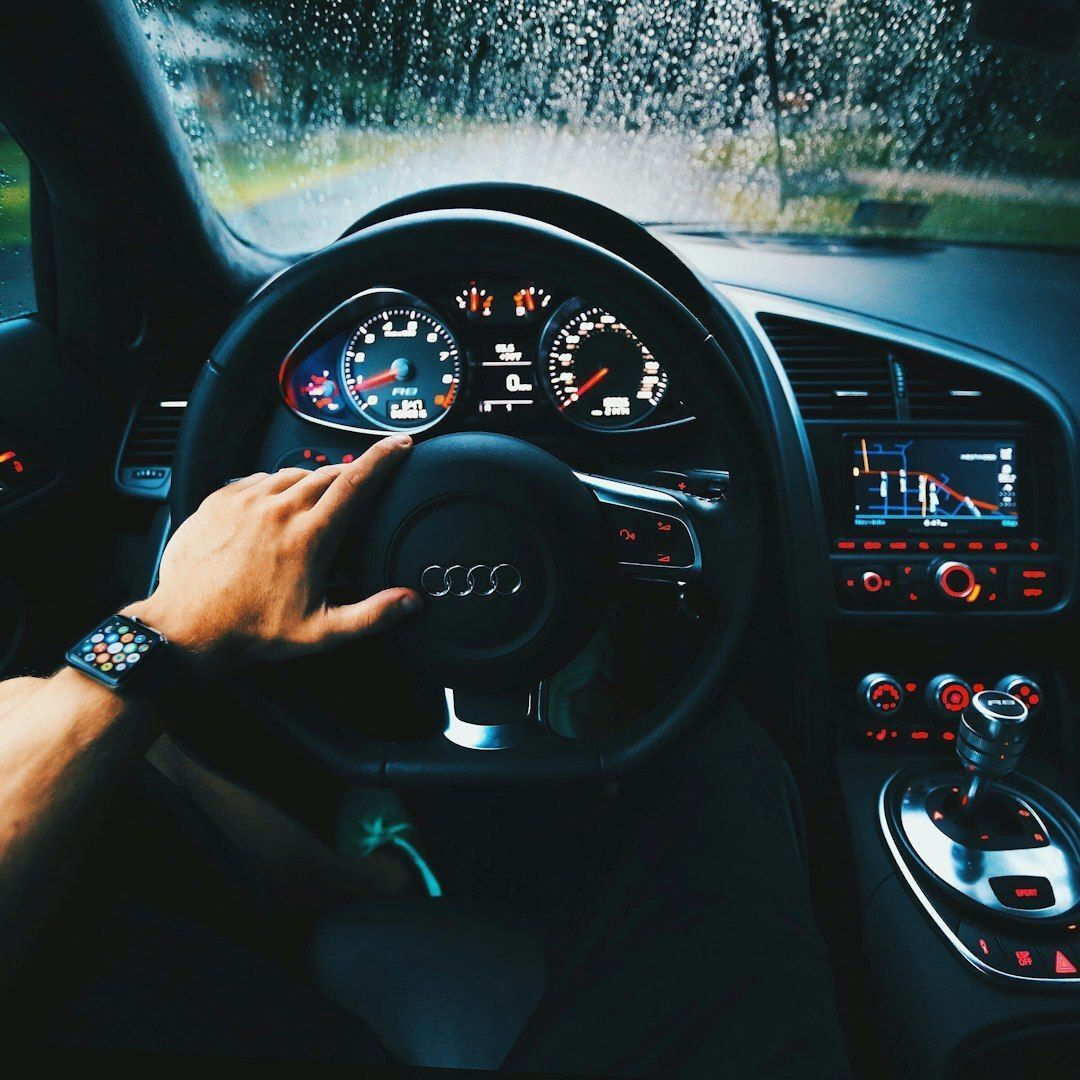 A driver's view from inside an Audi on a rainy day, with a hand resting on the steering wheel.