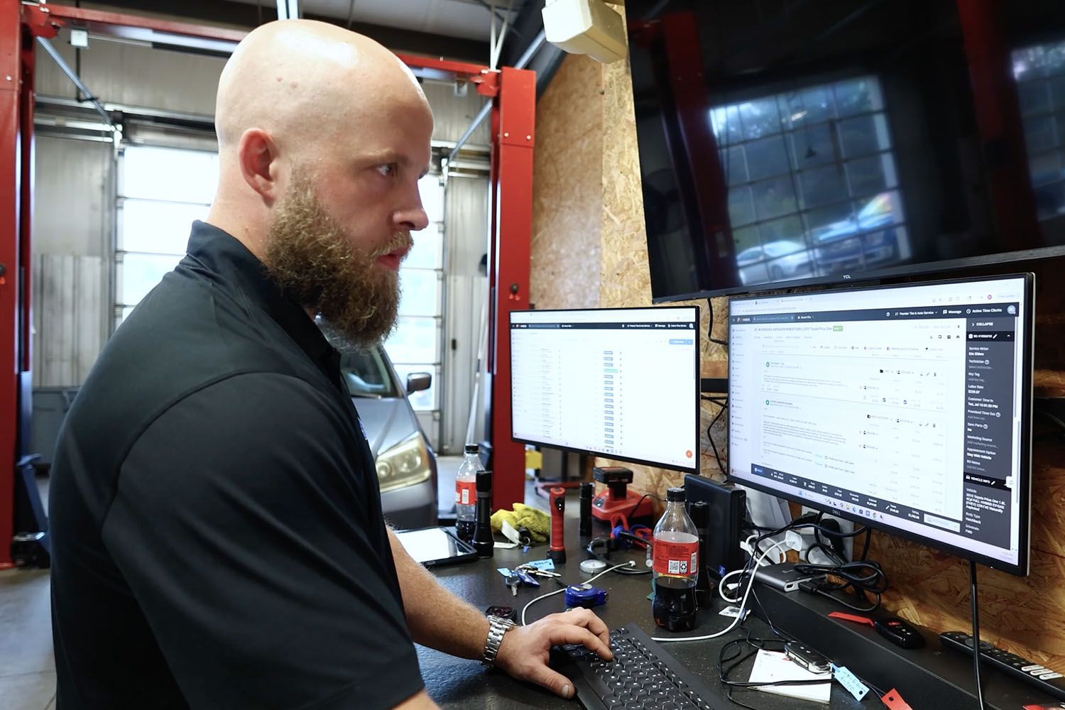 Man working at dual monitors in an industrial workshop, focused on a desktop computer.