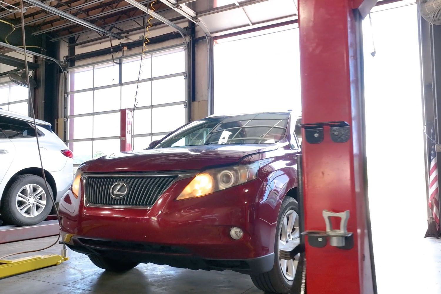 Red Lexus SUV in an auto repair garage, with a white car parked beside it.