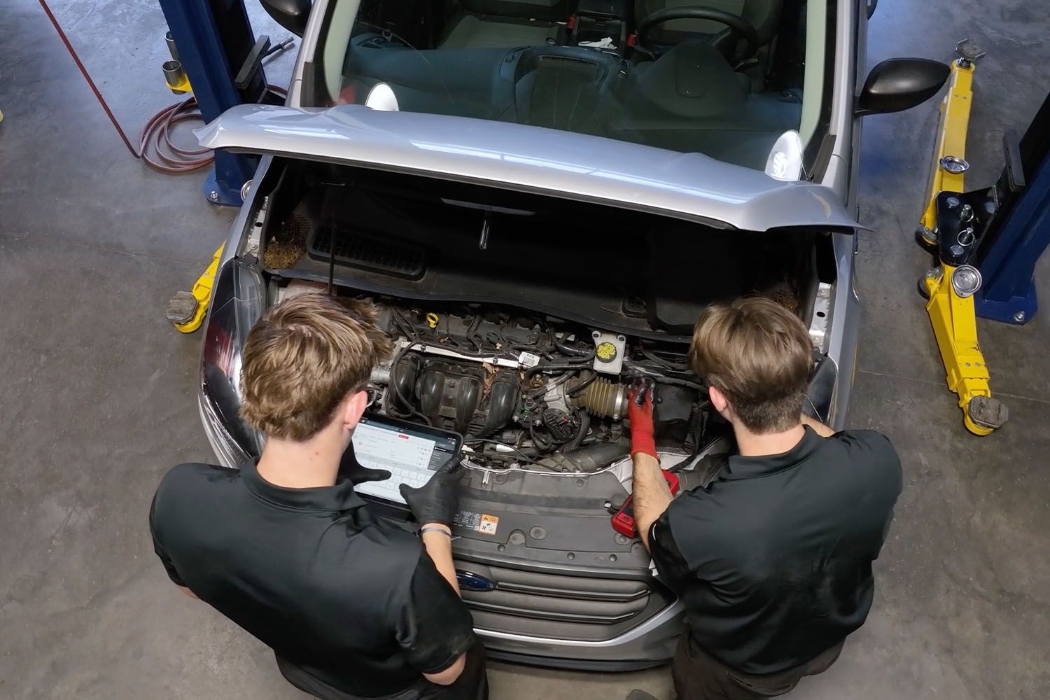 Two mechanics working under an open car hood in a garage