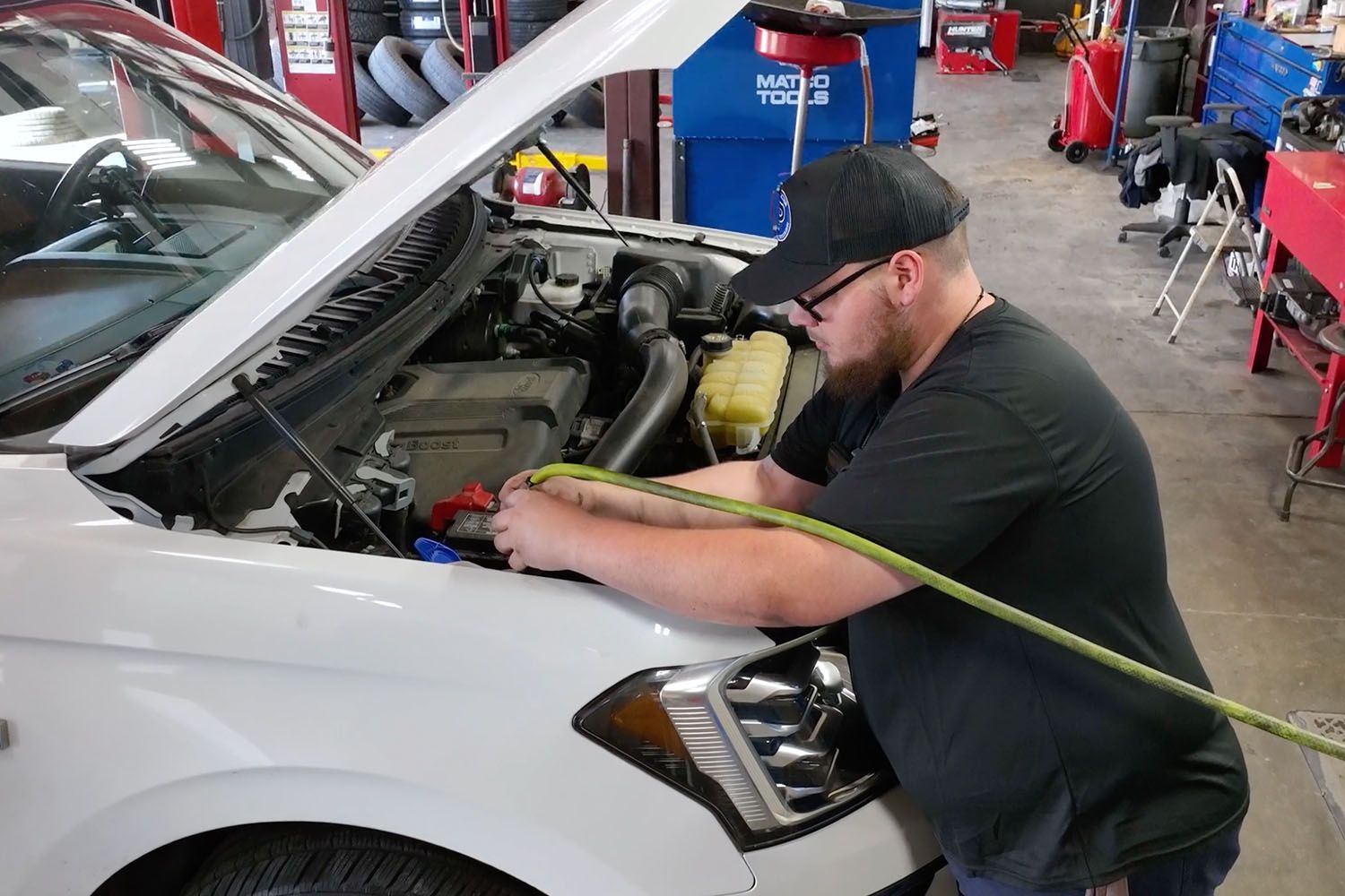 Mechanic working under an open car hood in a repair shop, using tools near the engine