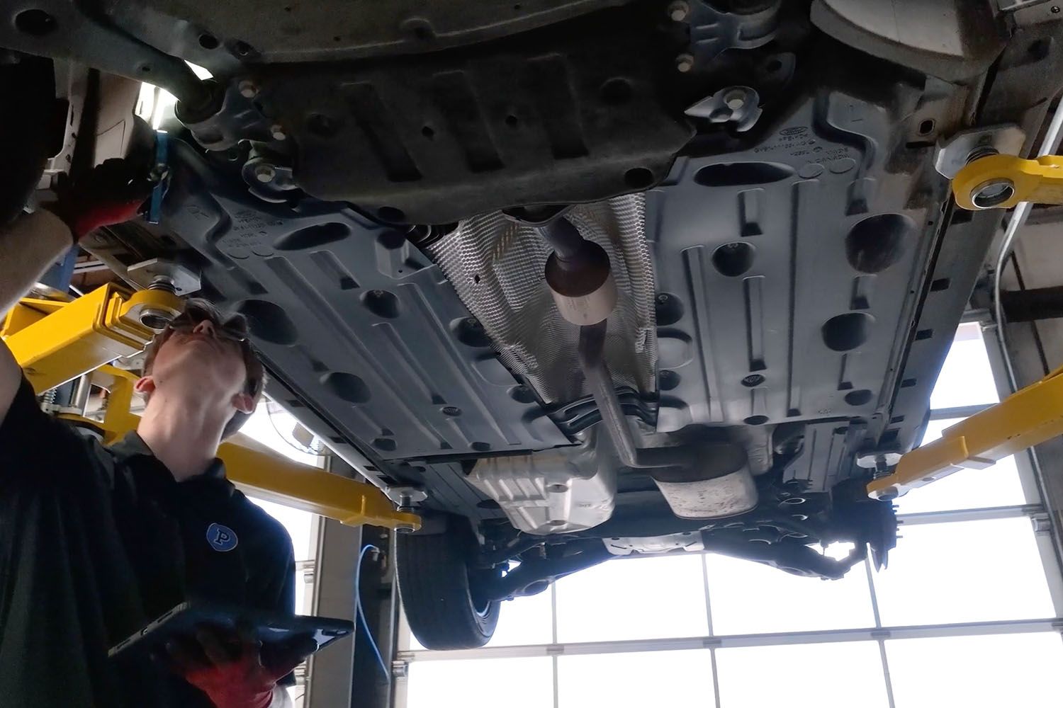 Mechanic inspecting the underside of a car on a lift in a garage
