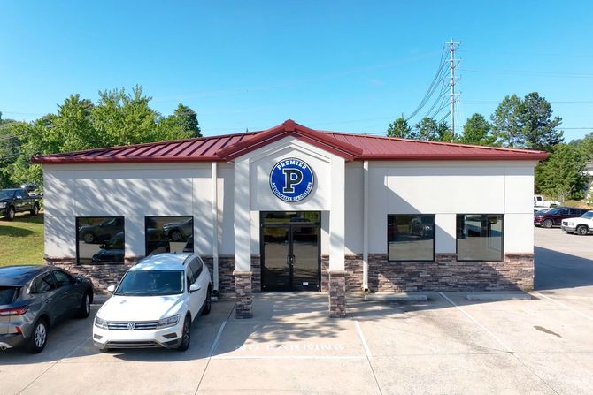 Front view of a white commercial building with red roof and parked cars under a blue sky