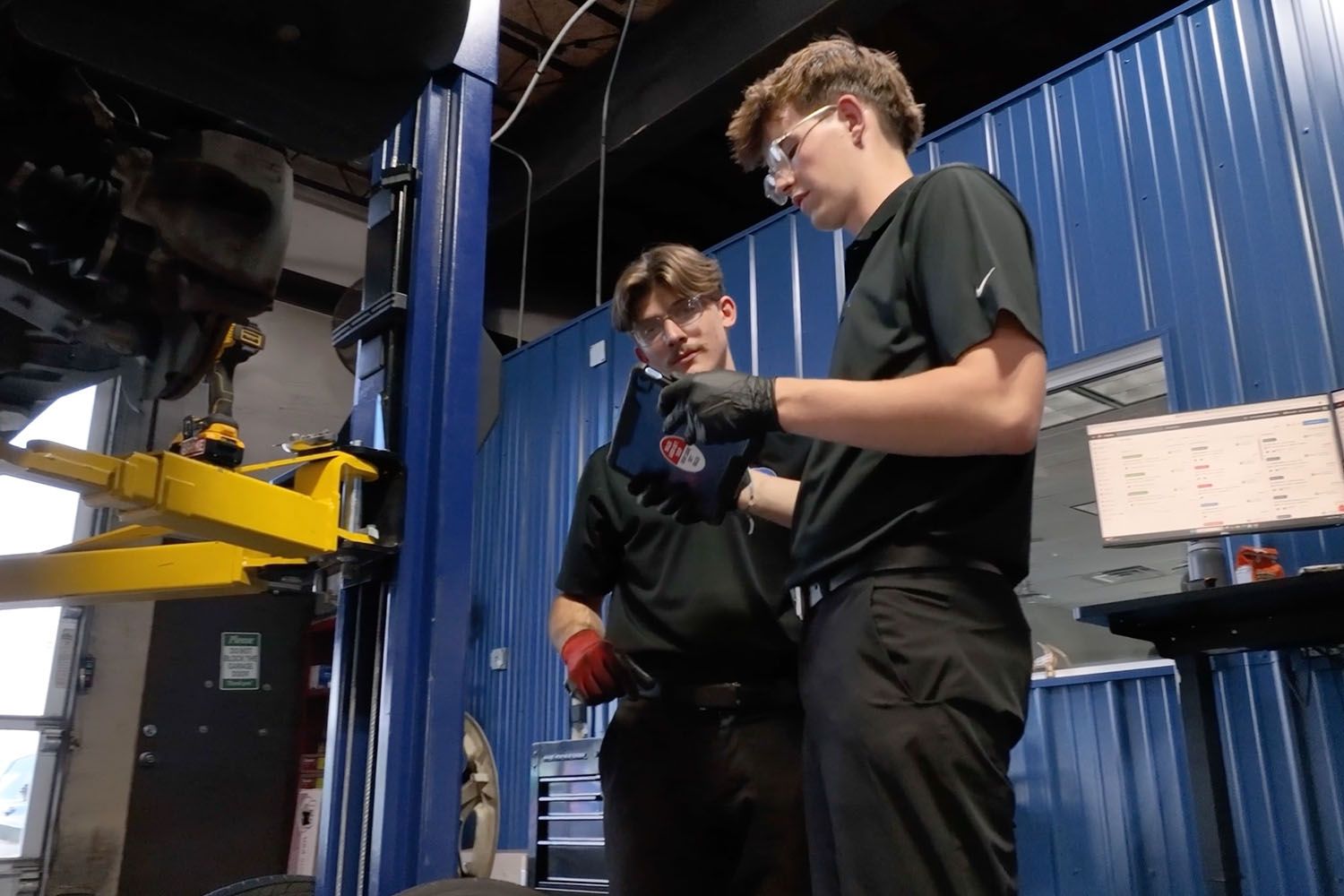 Two workers in black clothing inspecting equipment in a blue industrial workshop