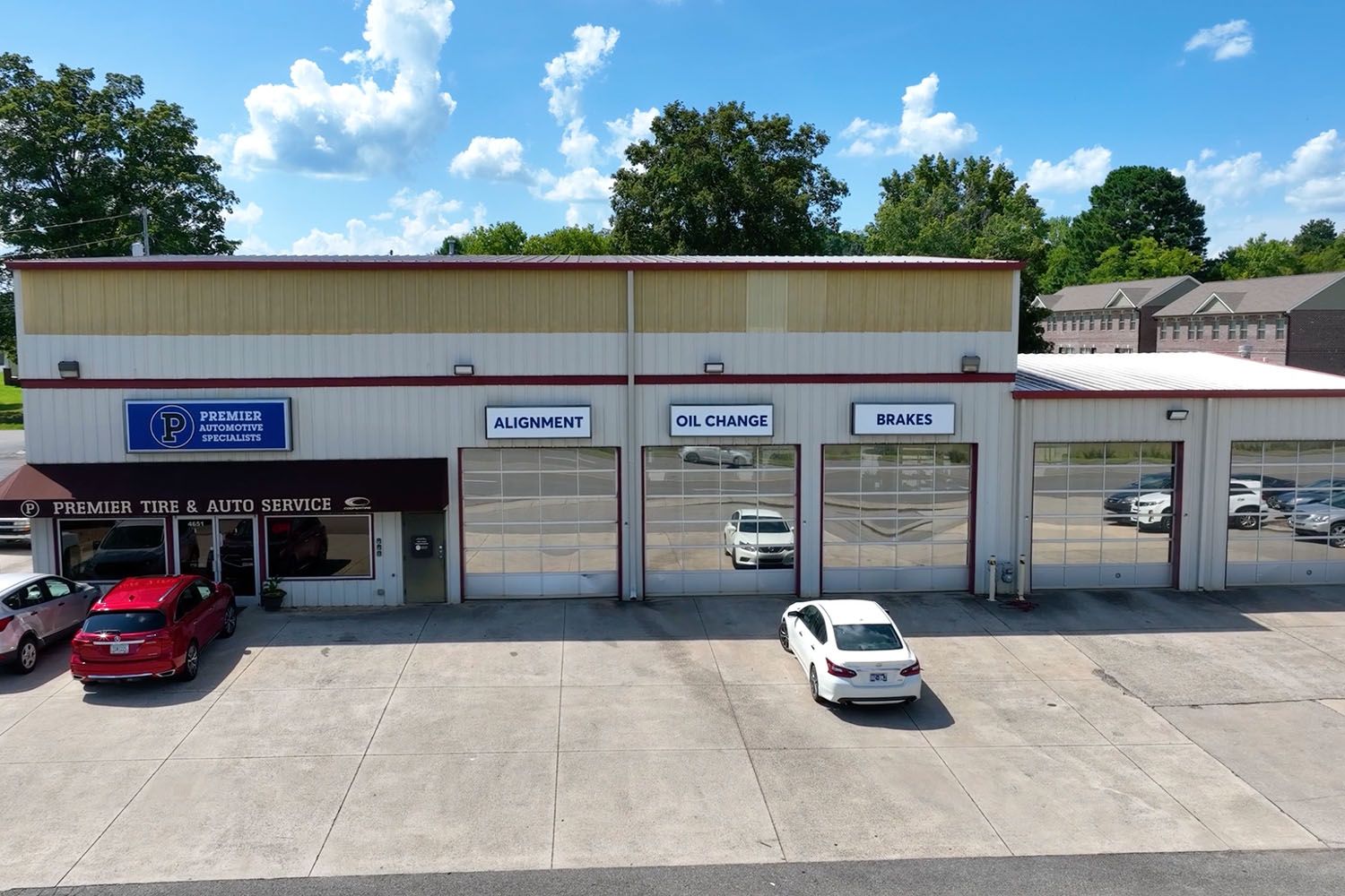 Auto repair garage with open bays, parked cars, and a partly cloudy sky