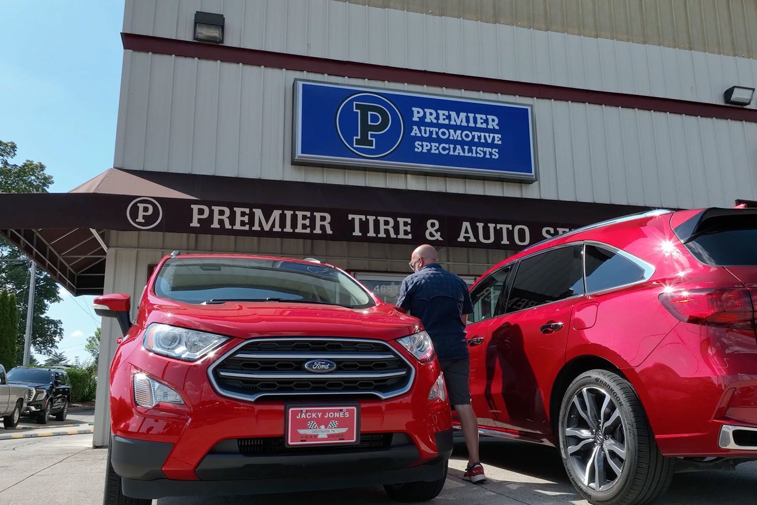 Two red cars parked outside Premier Tire & Auto Service, with a man standing between them