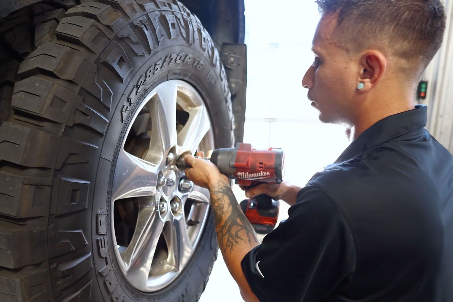 Mechanic using a red impact wrench on a truck’s front wheel in a garage