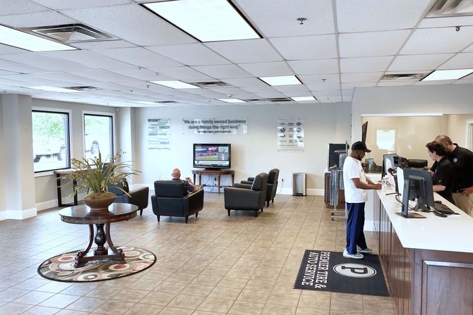 Bright hotel lobby with seating area, front desk, TV, and a few people near the check-in counter.
