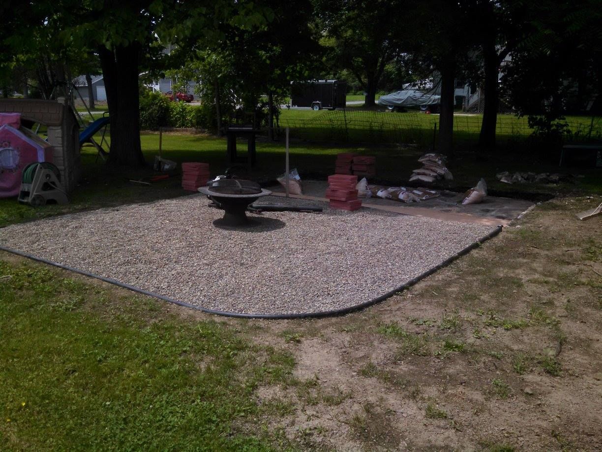 Gravel seating area in a shaded yard with a central fire pit and benches around a square border
