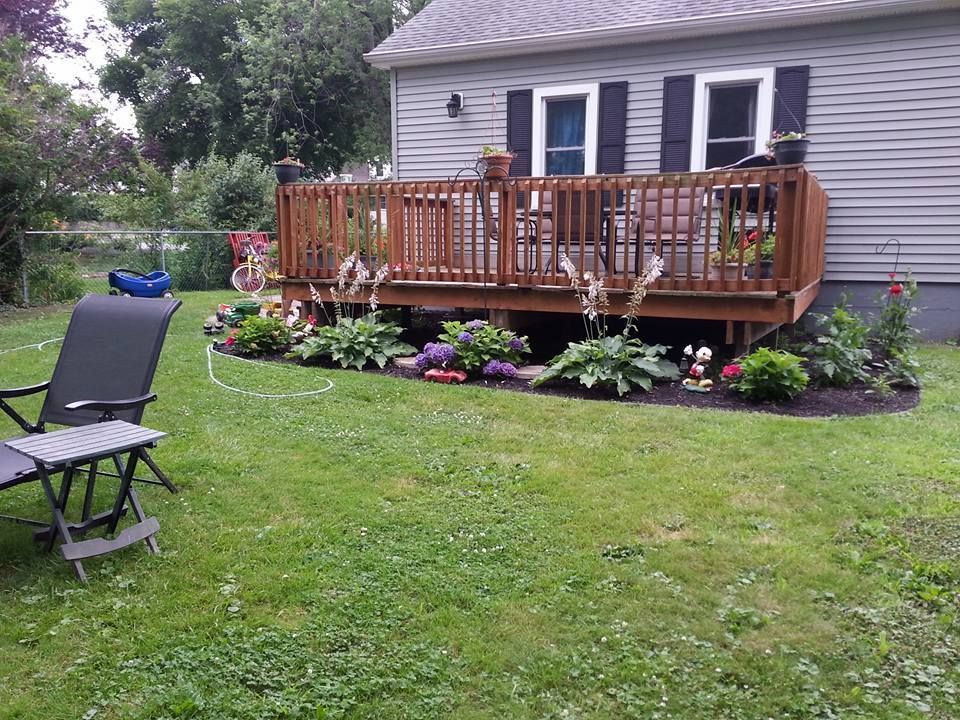 Backyard with a wooden deck, flower beds, and a lounge chair on the lawn.