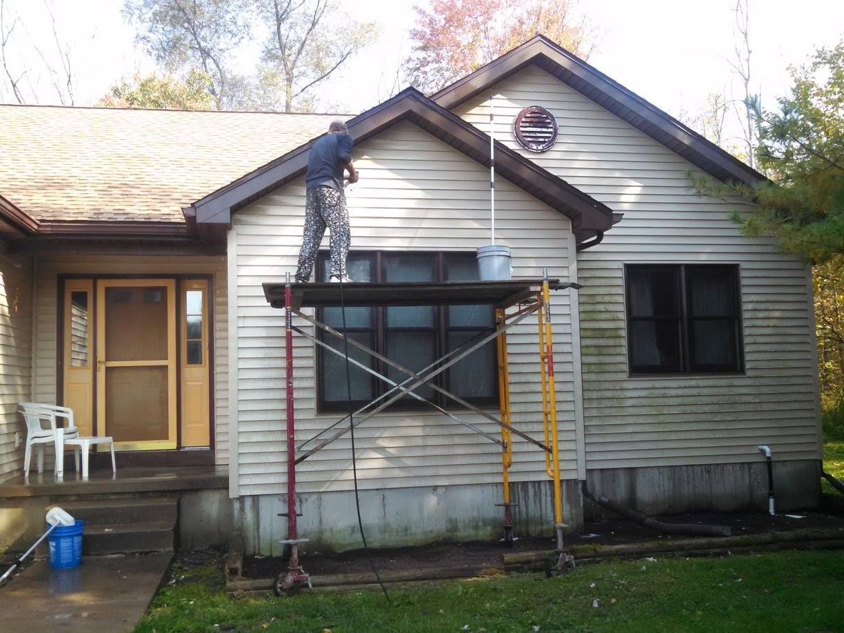 House exterior with a worker on a ladder repairing siding above a front porch scaffold