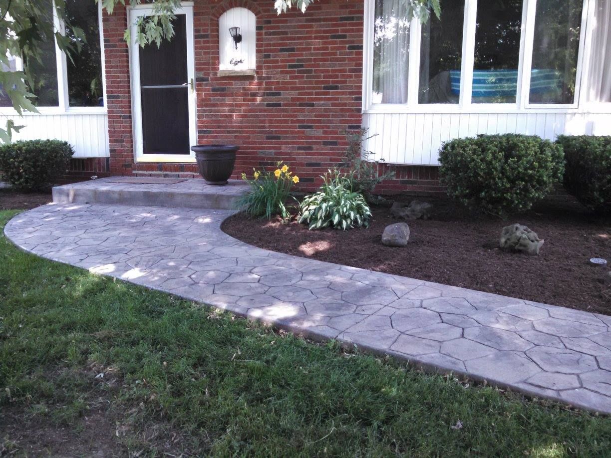 Front yard with a curved stone walkway, brick house entrance, and flower bed with shrubs and plants