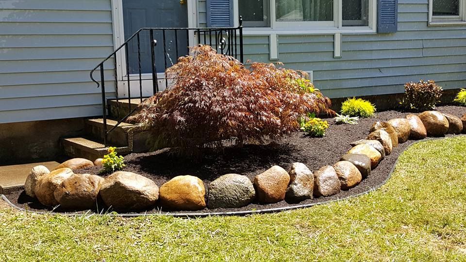 Rock garden border with rounded stones, shrubs, and mulch along a house foundation
