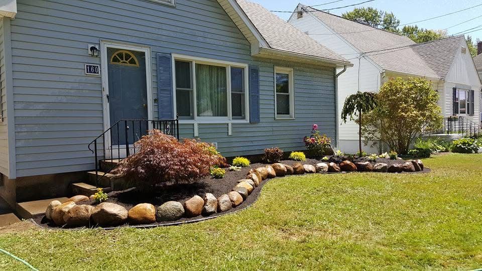 Blue house with a stone-edged flower bed and green lawn in front