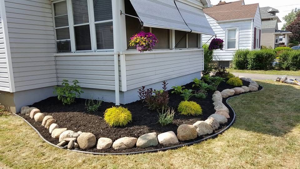 Front yard landscaping with curved stone border, black mulch, flowers, and a house porch