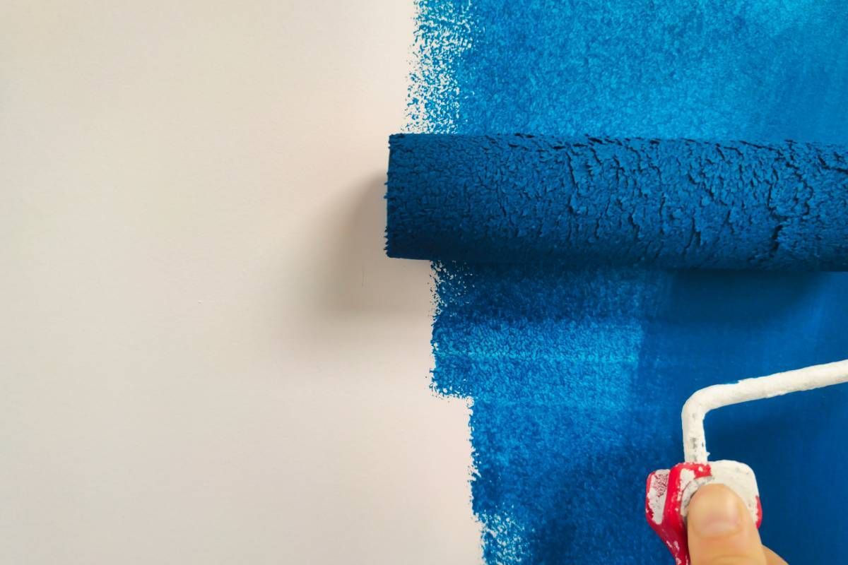 Close-up of a roller brush covered in blue paint being used to paint a wall