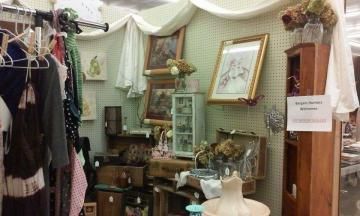Vintage clothing boutique with green curtains, framed art, dresses on racks, and decorative shelves