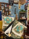 Quilt shop display with blue walls, patchwork quilts, baskets, and shelves of handmade decor
