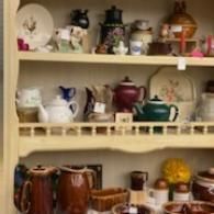 Shelves of assorted teapots and decorative ceramic dishware in a cozy display cabinet