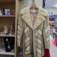 Beige faux-fur striped coat on a hanger in a store aisle