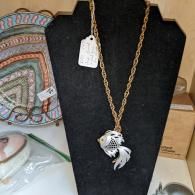 Gold chain necklace with silver fish pendant on a black display bust.