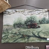 Red tractor in a green field with tree-lined background and dark tire tracks in the foreground