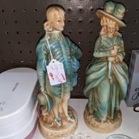 Pair of porcelain figurines in blue-green clothing on a shelf, one with a price tag attached