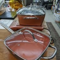 Two lidded stainless steel buffet serving dishes on a counter, with copper-colored interiors.
