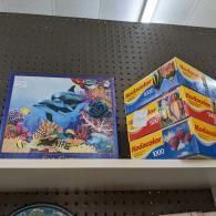 Shelf with two colorful puzzle boxes, including a blue dolphin scene and a stacked blue-and-yellow box set.