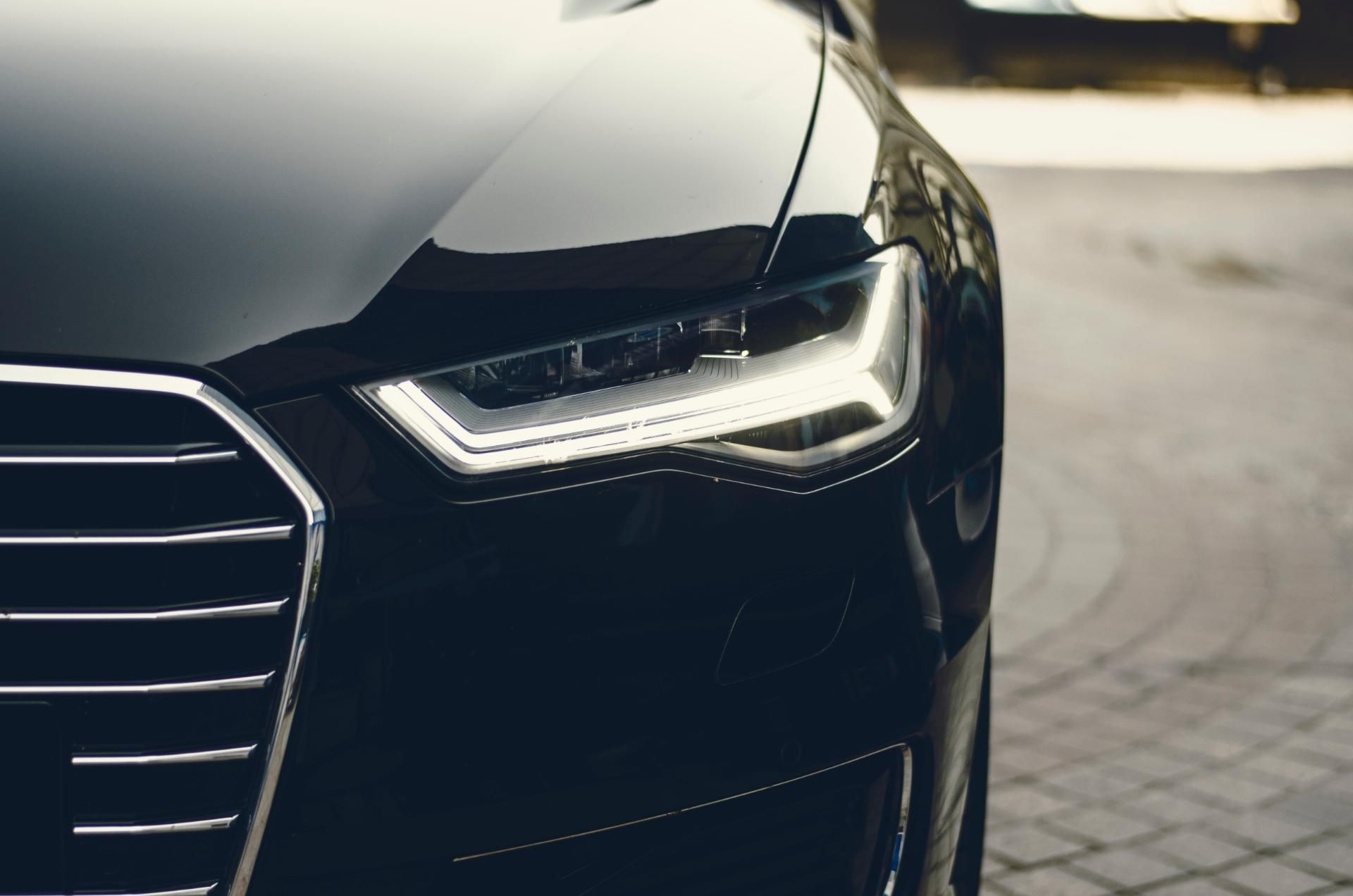 Close-up of a black car’s front grille and LED headlight on a paved street