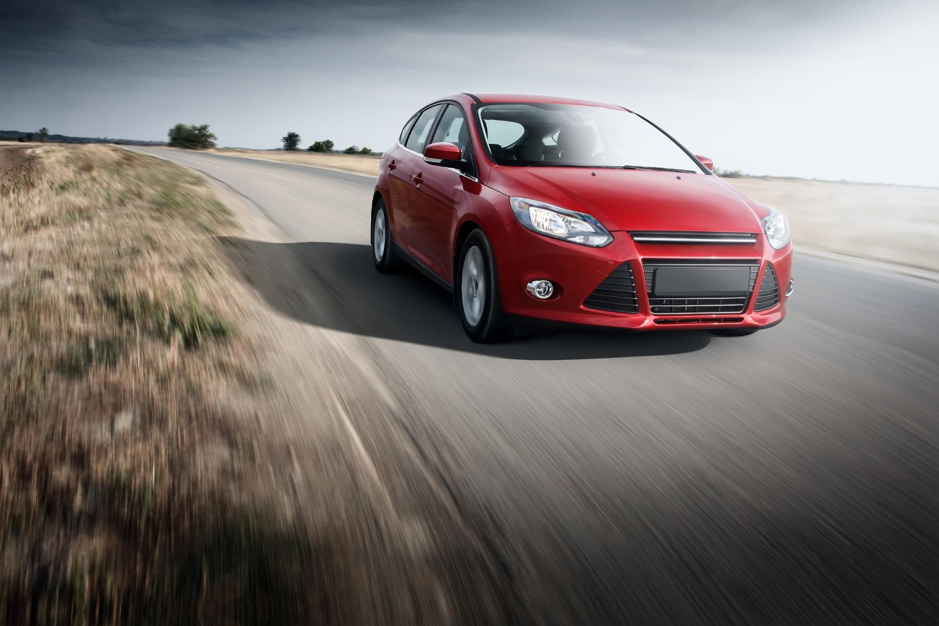 Red sedan driving fast on a winding road through a grassy landscape