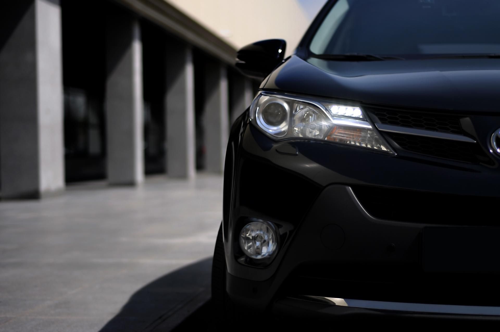 Close-up of a black car’s front corner parked beside concrete columns in a shaded area