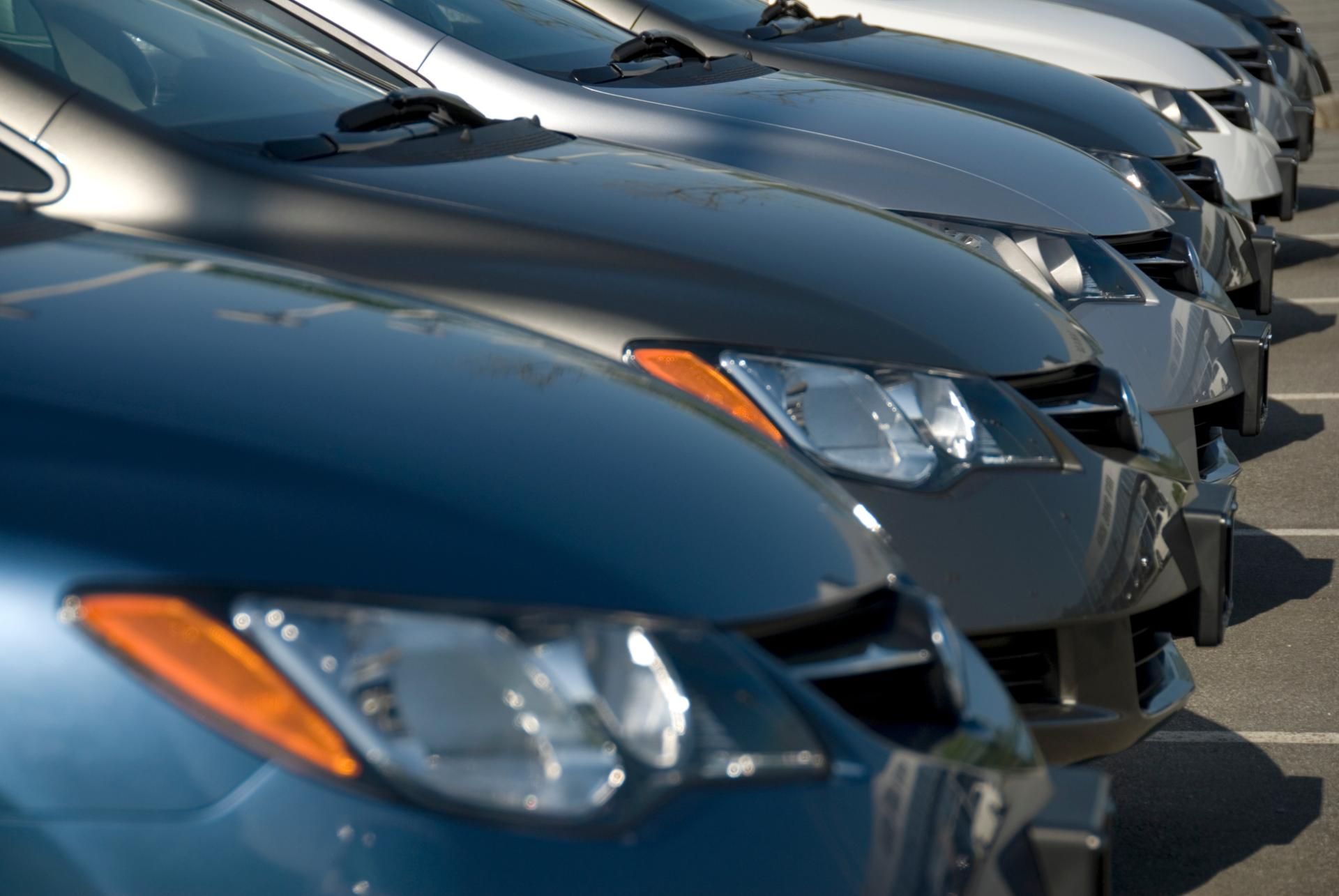 Row of parked dark blue cars viewed from the front at a dealership lot