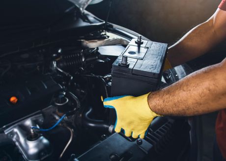Mechanic wearing yellow gloves working under a car hood in a garage