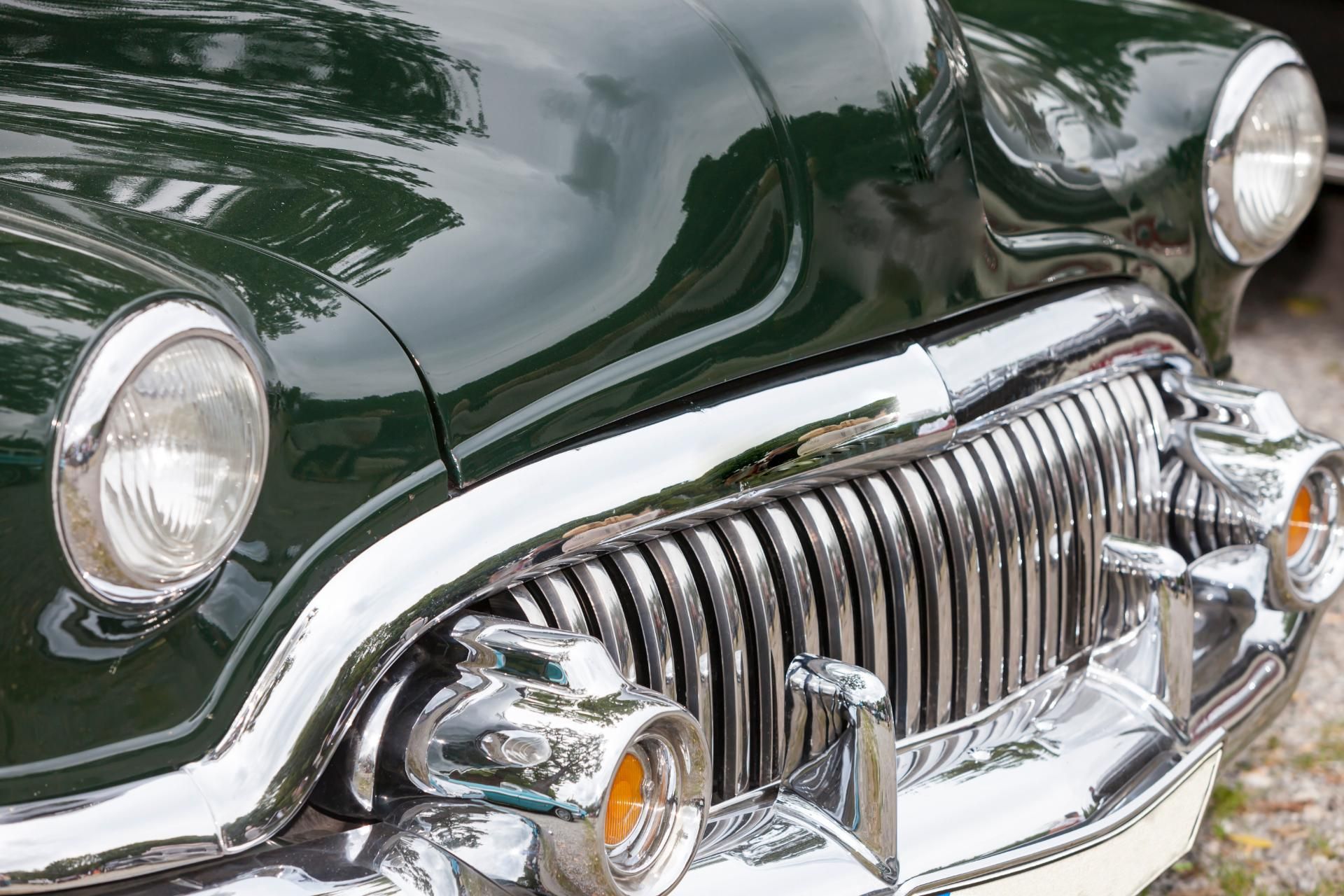 Close-up of a dark green vintage car’s chrome grille and headlights