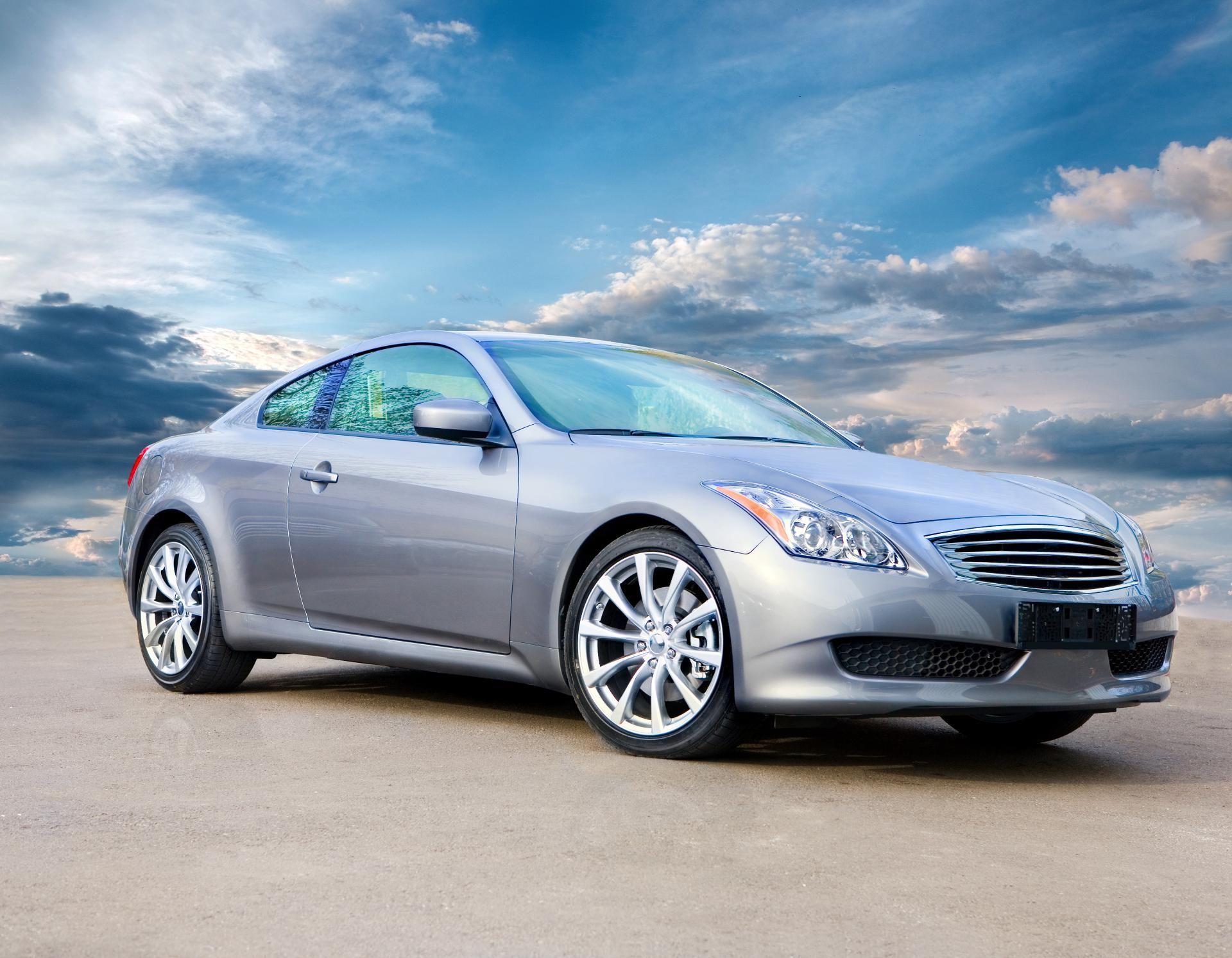 Silver coupe parked on a road under a cloudy blue sky