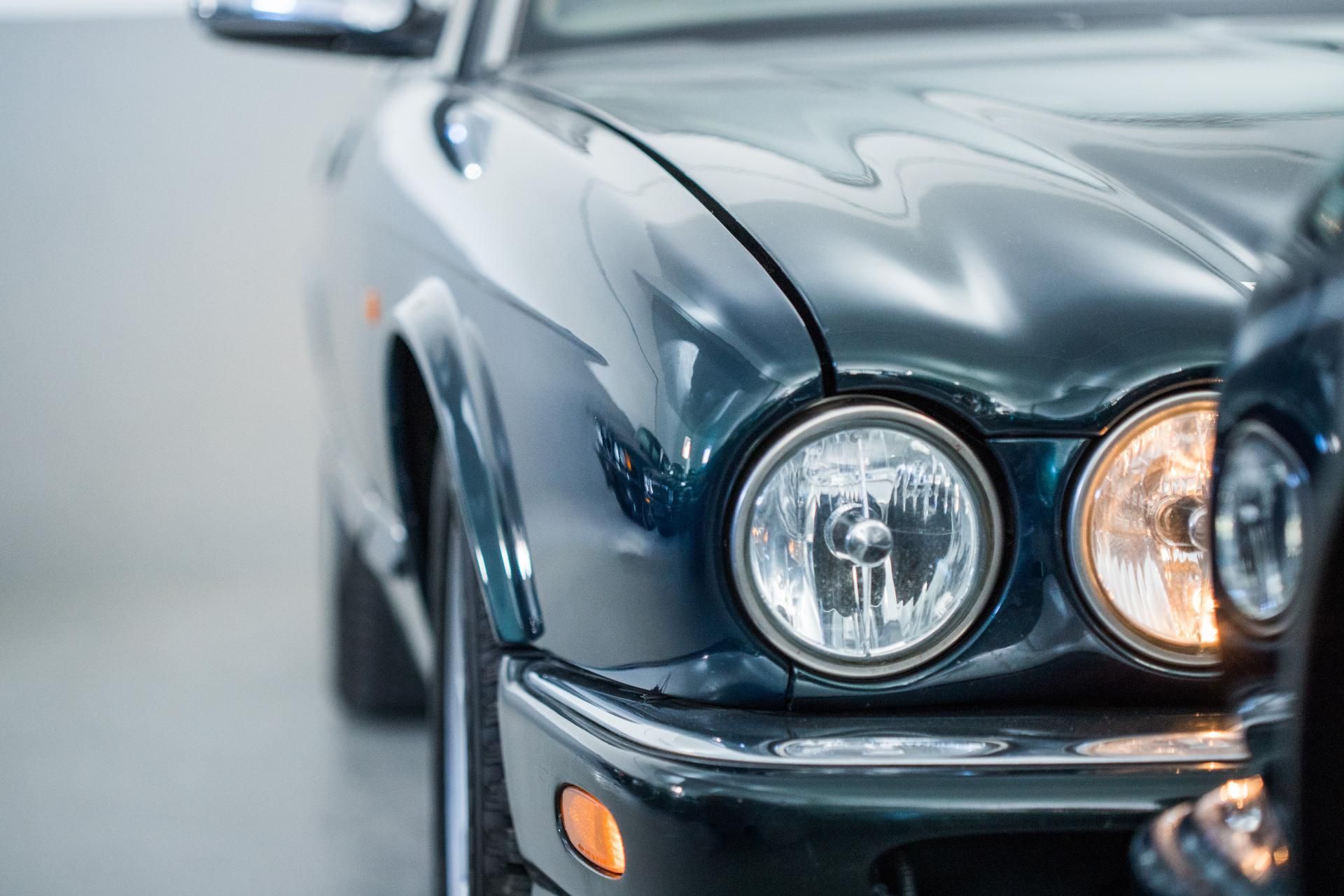 Close-up of a shiny black classic car’s front headlight and hood in a garage