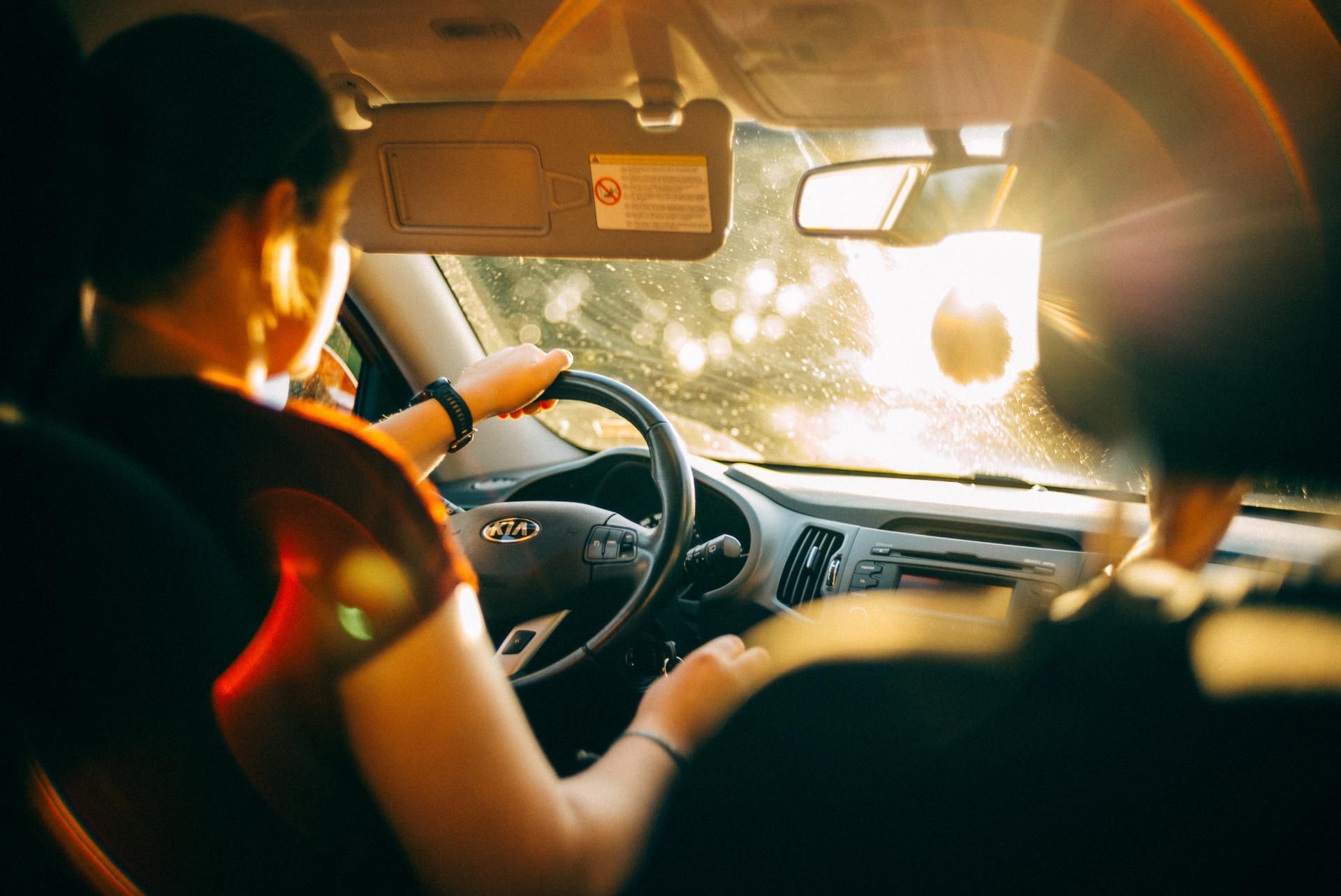 Two people driving a car at sunset, sunlight streaming through the windshield