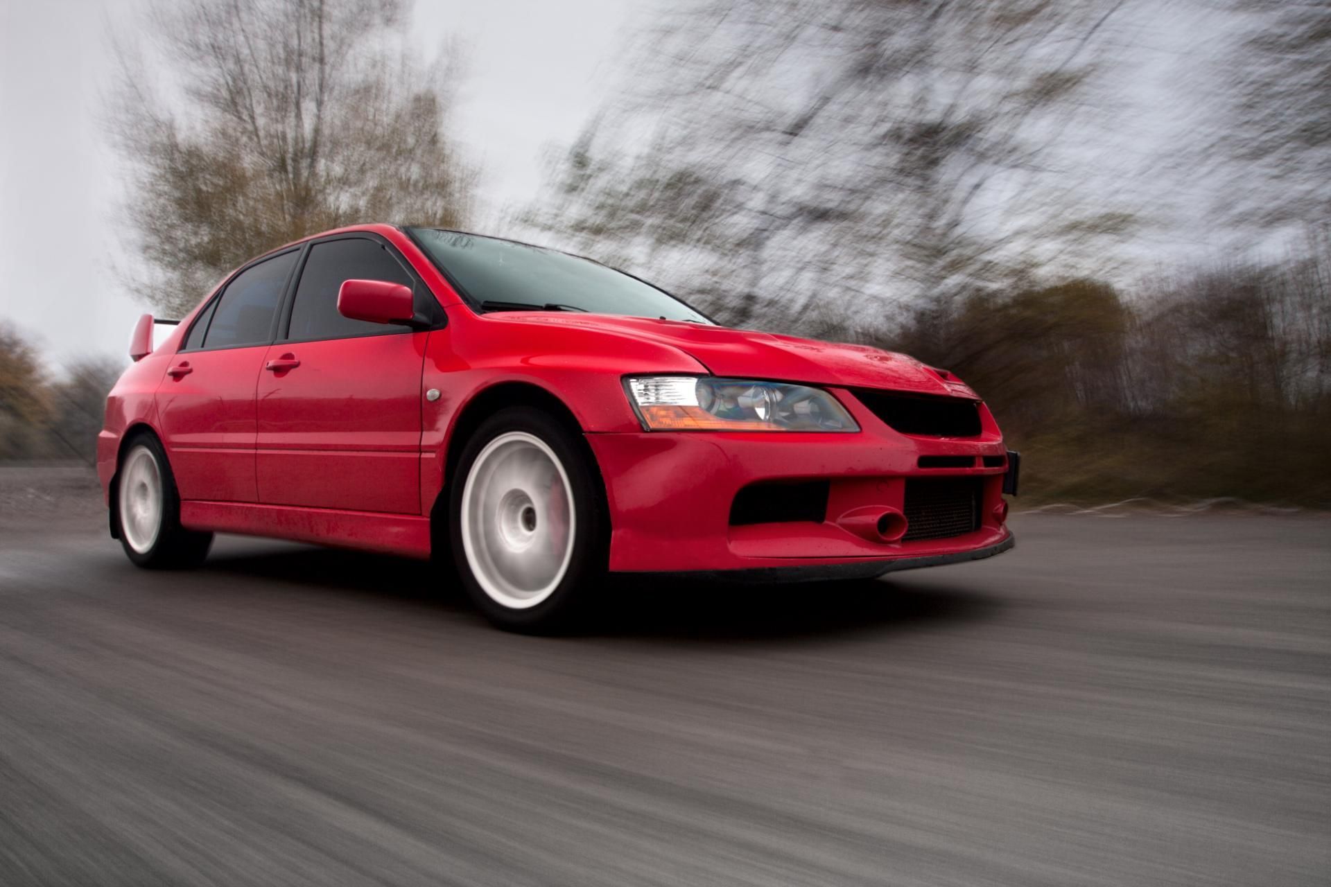 Red sports sedan speeding on a road with blurred trees in the background