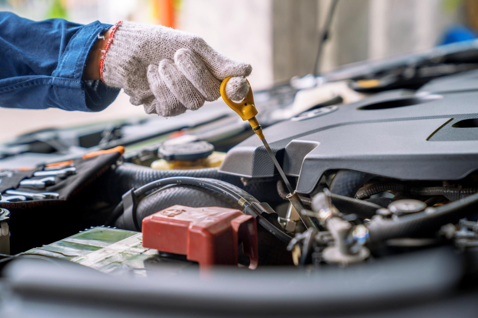 Gloved hand checking engine oil with a dipstick in a car engine bay