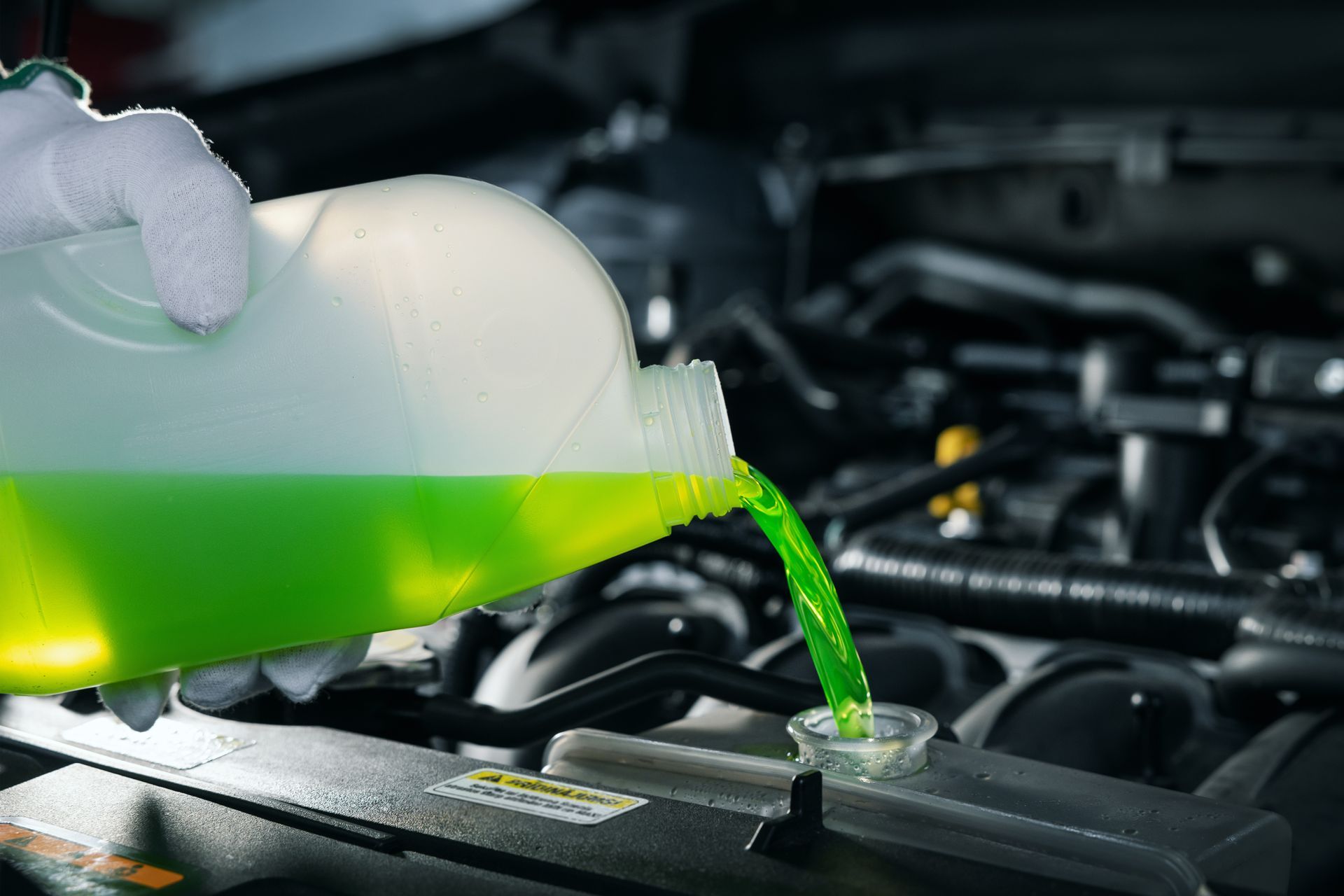 Gloved hand pours bright green coolant into a car engine reservoir